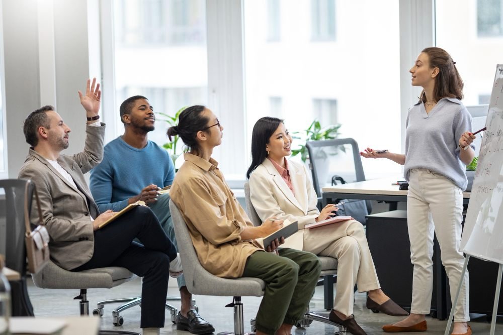 Reuni&atilde;o de equipe em ambiente corporativo com uma mulher apresentando ideias para colegas sentados, promovendo colabora&ccedil;&atilde;o e discuss&atilde;o estrat&eacute;gica.