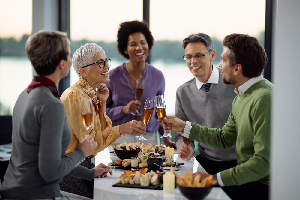 Grupo de profissionais de diferentes idades brindando com ta&ccedil;as de vinho durante um encontro social em ambiente corporativo