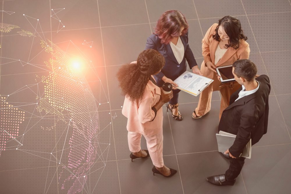 Grupo de profissionais discutindo estrat&eacute;gias de tecnologia e inova&ccedil;&atilde;o em um ambiente corporativo, com gr&aacute;ficos e dispositivos eletr&ocirc;nicos.