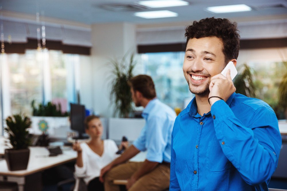 Profissional sorrindo ao telefone em um escrit&oacute;rio, representando um ambiente positivo gerado pelo desenvolvimento de lideran&ccedil;as.